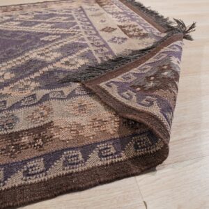Purple and brown geometric rug with visible fringes, partially folded back on light wood planks.