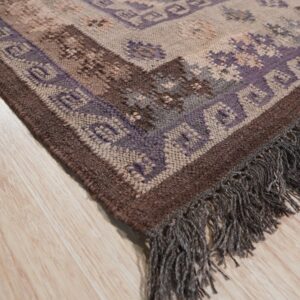 Textured rug with purple, brown, and beige geometric patterns, featuring fringe, lying on light wood flooring.