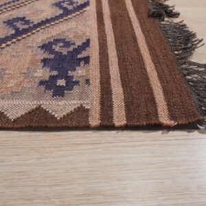 Geometric flatweave rug with purple patterns, brown stripes, and dark fringe rests on light wood planks.