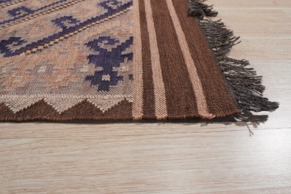 Geometric flatweave rug with purple patterns, brown stripes, and dark fringe rests on light wood planks.