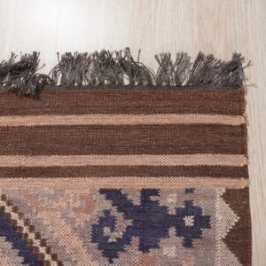 Brown and tan striped flat-weave rug with blue geometric details and dark fringe on light wood floor.