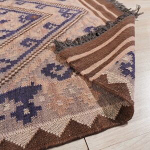 A purple and tan geometric rug is folded on light flooring, showing a striped brown backing and fringe.