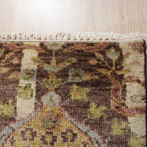 Close-up of a high-pile, brown, cream, and multicolor patterned rug with fringe on light wood flooring.