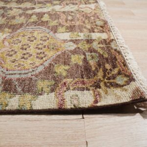 Textured traditional rug in brown, gold, cream, and rose with fringe detail on light wood plank flooring.
