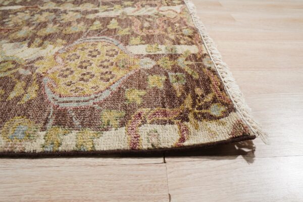 Textured traditional rug in brown, gold, cream, and rose with fringe detail on light wood plank flooring.
