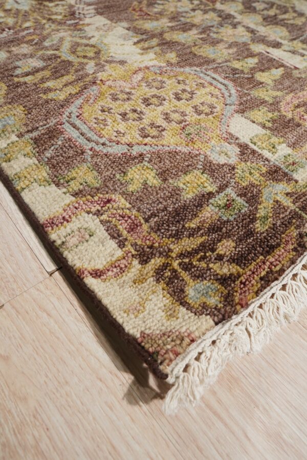 A chunky-pile rug with brown, cream, and gold traditional patterns and fringe rests on light plank flooring.