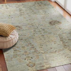 Muted blue rug with tan and brown traditional patterns rests on dark hardwood flooring near a pleated pouf.