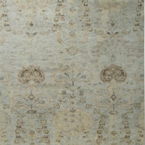 Low pile rug in muted gray-blue, cream, and brown with repeating traditional floral patterns and white fringe.
