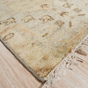Highly textured cream rug with tan geometric patterns and knotted fringe on light wood plank flooring.