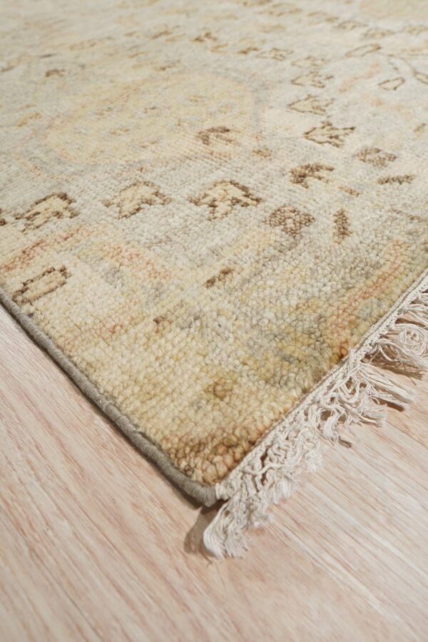 Highly textured cream rug with tan geometric patterns and knotted fringe on light wood plank flooring.