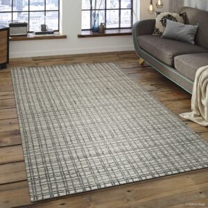 Textured gray and white grid pattern rug rests on distressed wood flooring by large industrial windows.