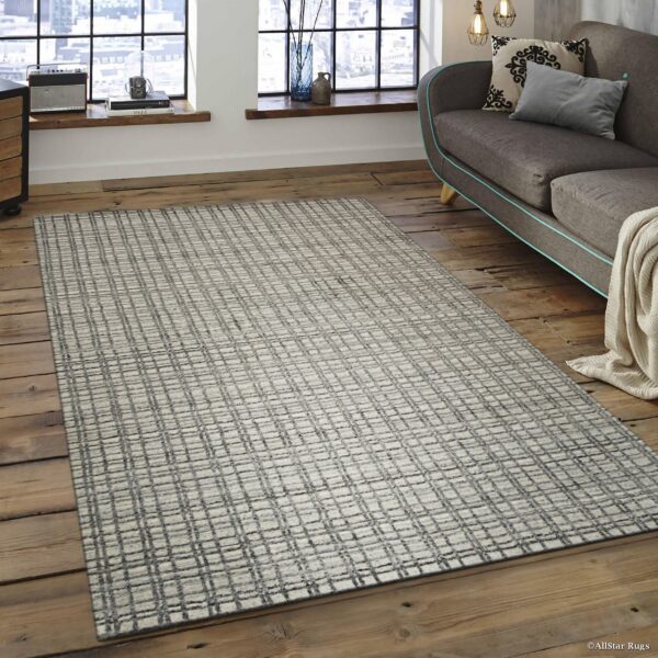 Textured gray and white grid pattern rug rests on distressed wood flooring by large industrial windows.