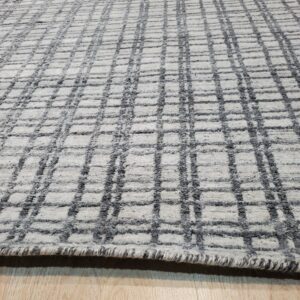 Textured gray and off-white rug with a geometric grid pattern lies on light wood flooring.