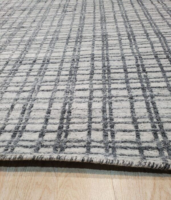 Textured gray and off-white rug with a geometric grid pattern lies on light wood flooring.