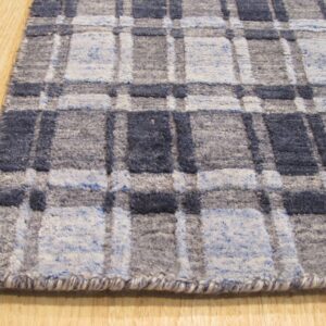 Close-up of a blue, light blue, and gray plaid rug with varied pile textures placed on a wooden floor.