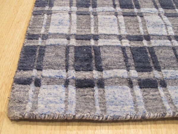 Close-up of a blue, light blue, and gray plaid rug with varied pile textures placed on a wooden floor.