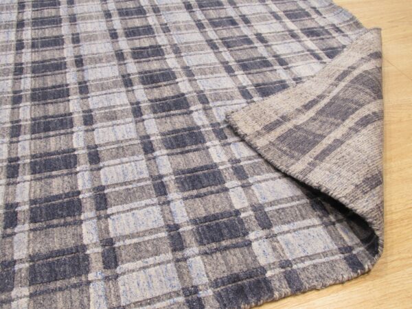 Blue and gray plaid rug lies on a light wood floor with the corner folded to show the backing.