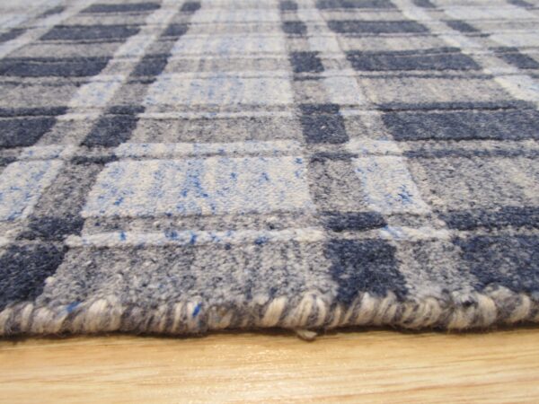 Textured blue and gray plaid rug with a visible rolled edge resting on light wood flooring.