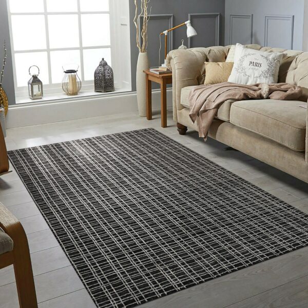 A textured black and white grid pattern rug sits under a tan sofa on light wood plank flooring.