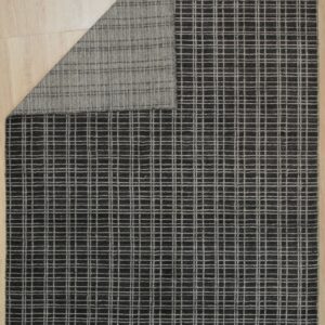 Dark charcoal rug with a light gray grid pattern on wood flooring, folded to show the woven backing.