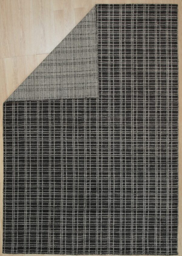 Dark charcoal rug with a light gray grid pattern on wood flooring, folded to show the woven backing.