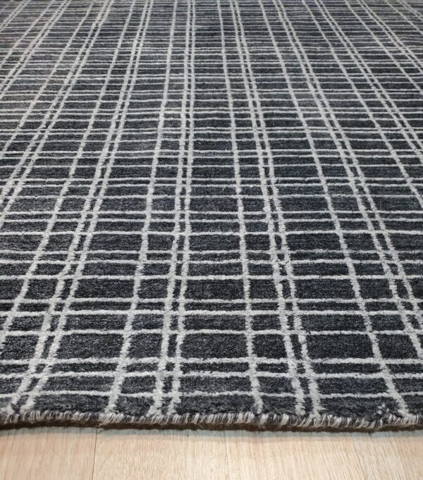 A textured charcoal and white rug with a grid pattern is displayed on light wood flooring.