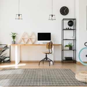 A dark gray grid rug anchors a bright modern home office with wood floors and a desk.