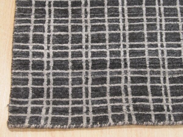 A dark mottled gray rug featuring a light gray windowpane check pattern rests on wood flooring.