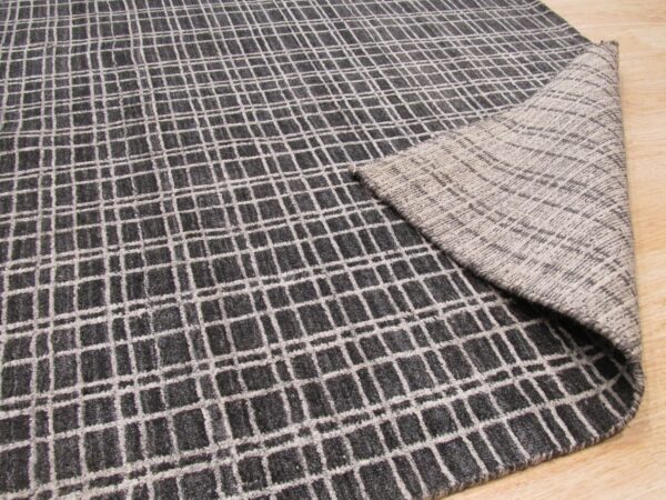 Textured gray rug with a white grid pattern, folded to show the lighter gray woven backing on wood.