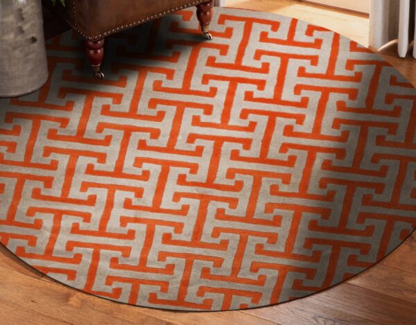 Circular rug featuring an orange fret pattern on a light gray background, beneath a studded brown chair leg.