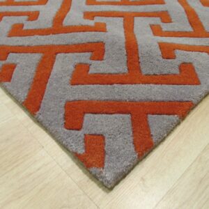 Deep pile gray rug with raised orange interlocking geometric patterns on light wood flooring.