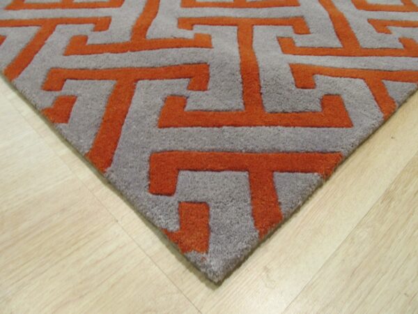 Deep pile gray rug with raised orange interlocking geometric patterns on light wood flooring.