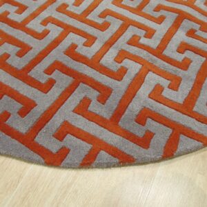 Round gray rug featuring a raised orange Greek key pattern on light wood flooring.