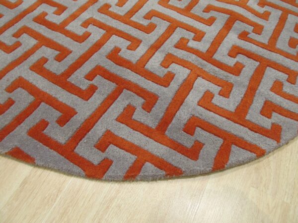 Round gray rug featuring a raised orange greek key pattern on light wood flooring.