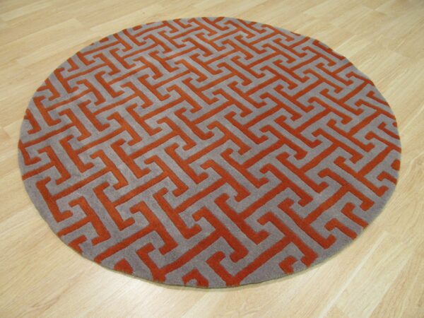 Round rug with a gray and terracotta geometric key pattern and visible texture on light wood flooring.