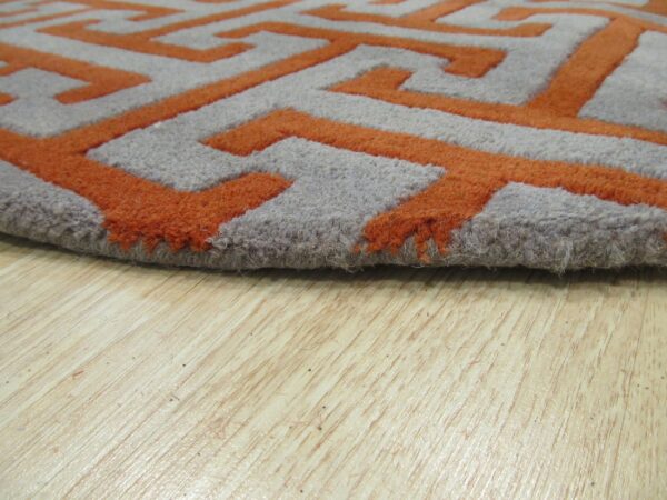 The thick pile of a bright orange and gray geometric rug rests on light wood flooring.