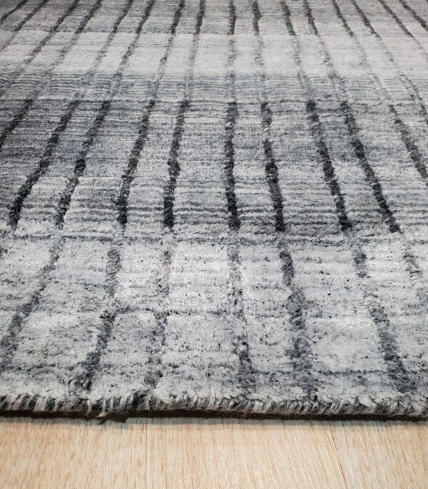 Textured, high-pile gray and white rug featuring a dark striped grid pattern over light wood flooring.