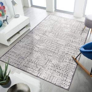 White rug featuring a textured, dark gray abstract geometric pattern rests on light wood plank flooring.