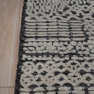 Shaggy cream and dark gray rug showing tiered abstract geometric patterns beside blonde wood flooring.