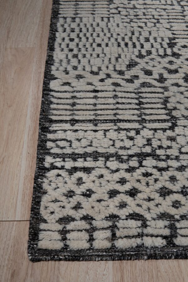 Shaggy cream and dark gray rug showing tiered abstract geometric patterns beside blonde wood flooring.