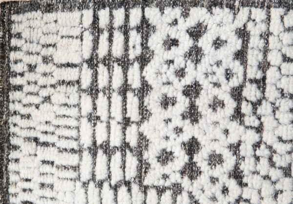Close-up view of a high-pile rug featuring an abstract geometric pattern in cream and speckled gray.
