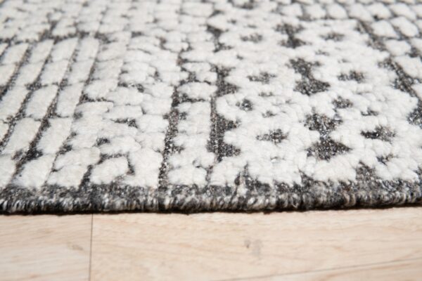Textured gray and cream rug with a raised geometric pattern displayed close-up on light wood flooring.