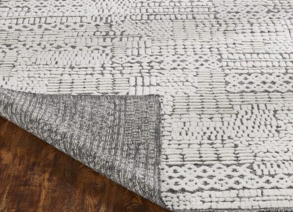 White rug with a high-low gray pattern lifted to show the woven backing and dark wood floor.