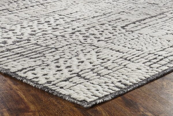Textured cream and dark gray rug featuring a raised geometric pattern on wood flooring.