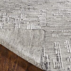 Textured gray and cream rug with geometric patterns displays its backing on dark brown wood floor.