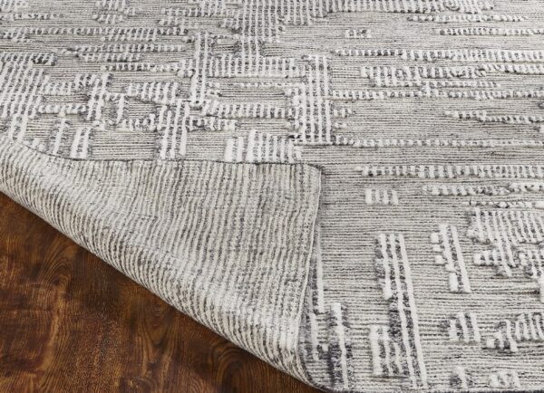 Textured gray and cream rug with geometric patterns displays its backing on dark brown wood floor.