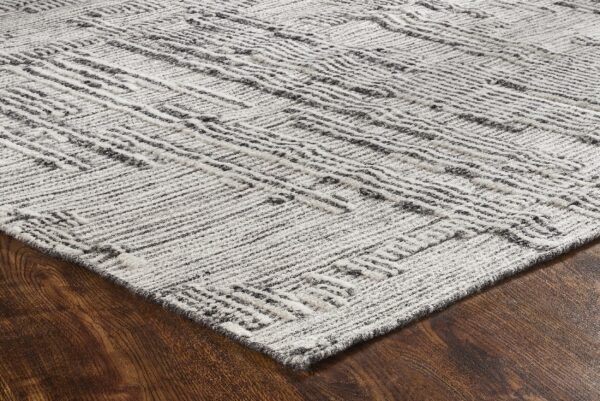 Textured gray and off-white rug with an abstract linear pattern rests on dark brown wood flooring.