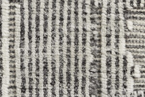 Detail view of a textured, high-pile rug showing irregular vertical stripes in black and fluffy white.