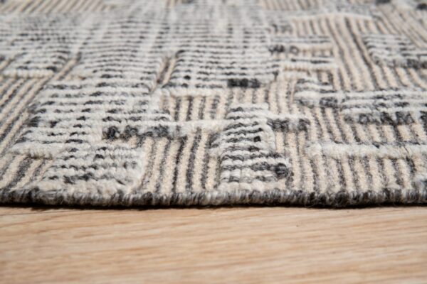 Textured cream and dark gray rug with a dimensional geometric pattern resting on light wood floor.