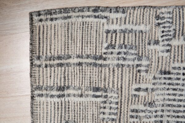 Cream and dark gray textured rug featuring vertical stripes and abstract geometric patterns on light wood flooring.